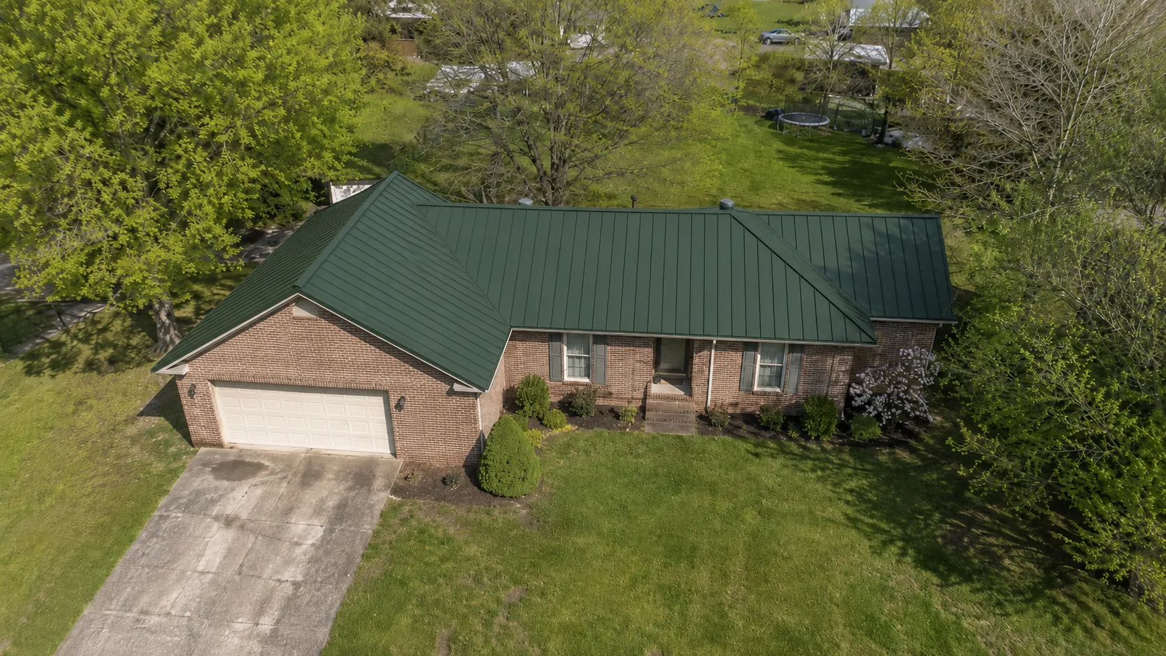 The same brick ranch home from above, now with a new dark green standing-seam metal roof