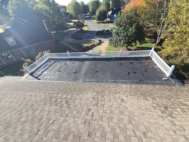Railed flat roof deck with its old dark membrane, set into a shingle roof in Mayfield, KY, before replacement