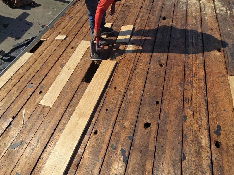 Roofer cutting new boards into an old plank roof deck during a tear-off in Reidland, KY