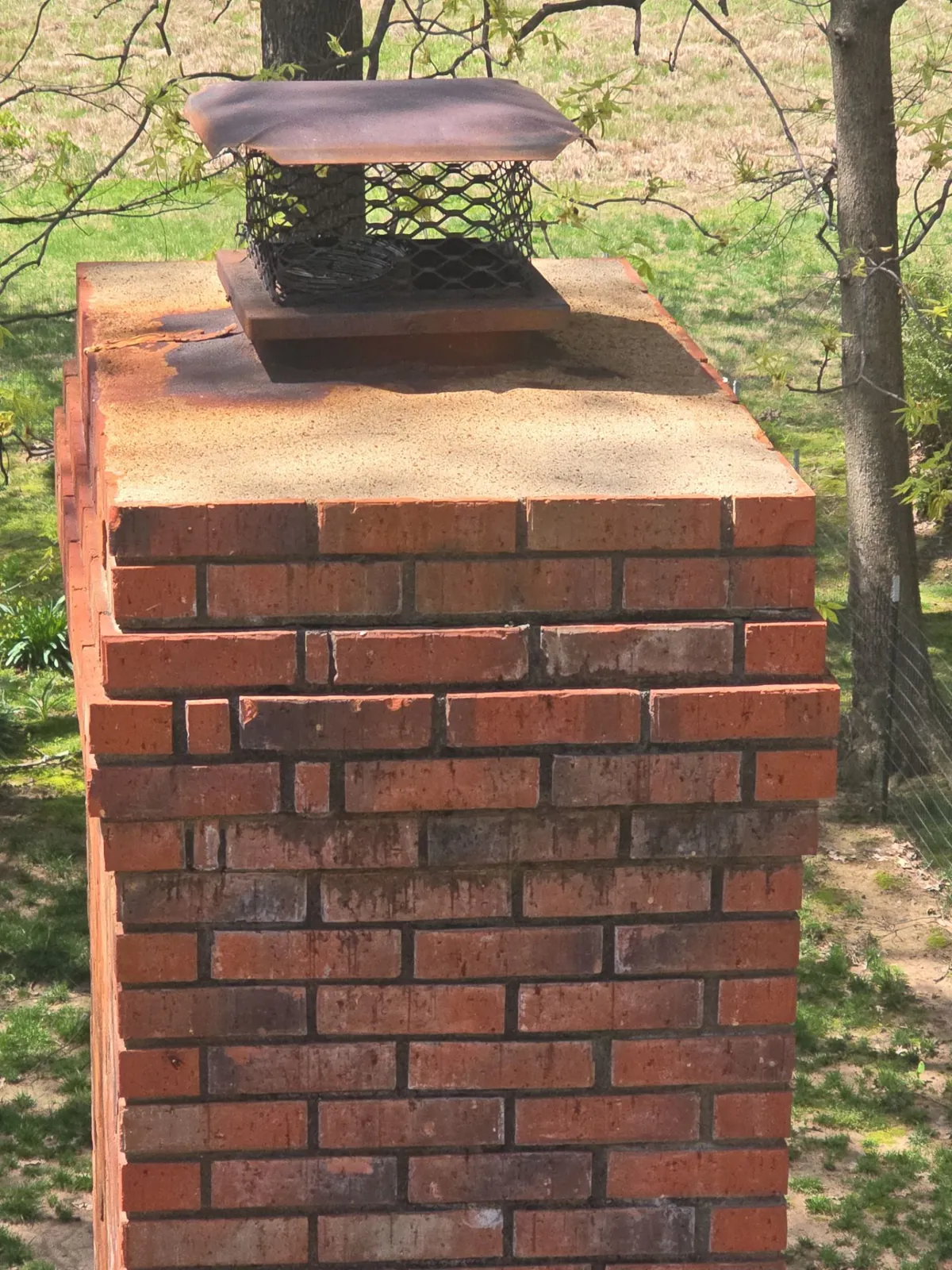 Brick chimney in Hazel, KY with a weathered, stained crown and mesh cap, before repair