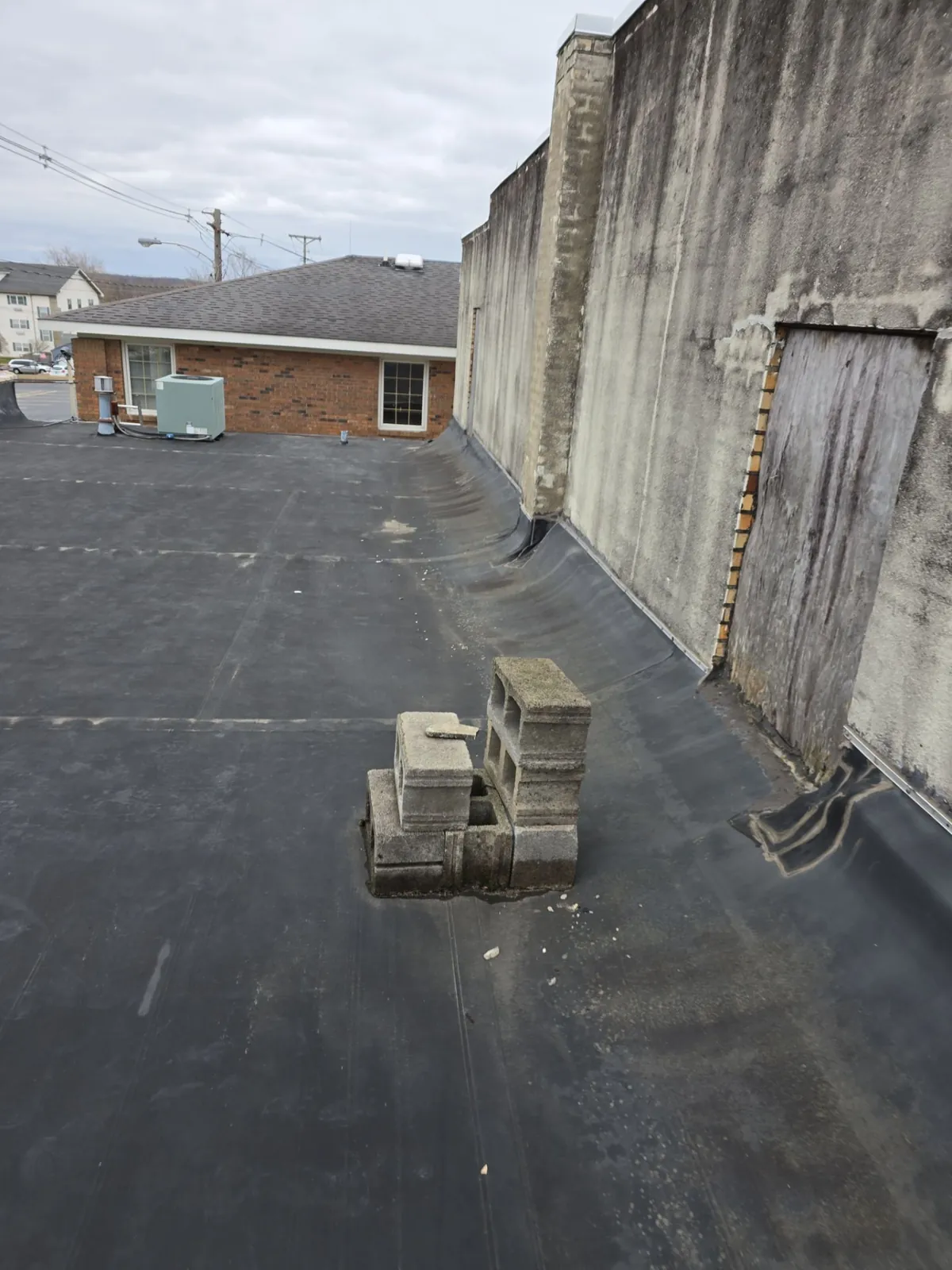 Old dark membrane flat roof running along a tall masonry wall, before replacement