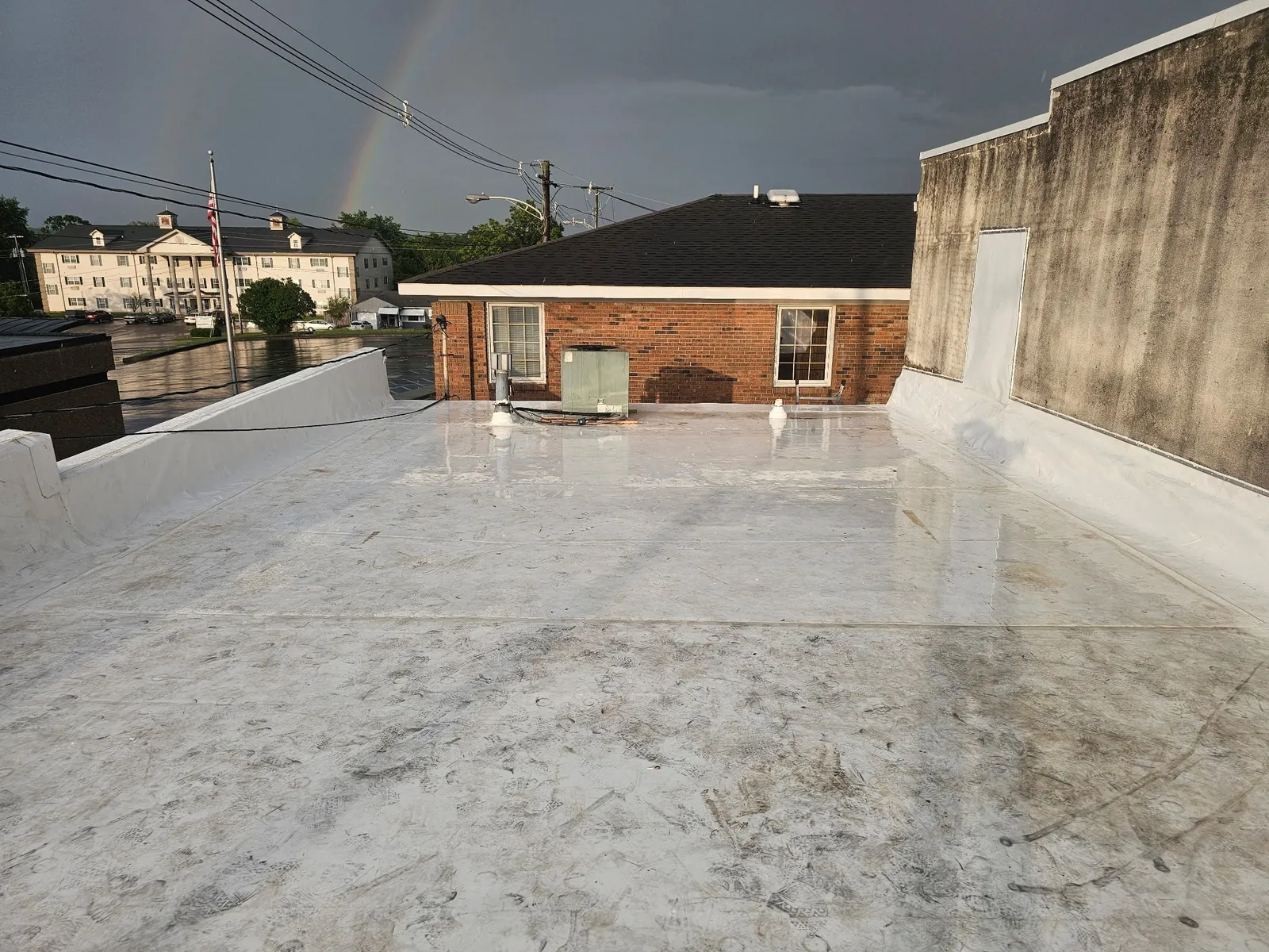 The finished white single-ply membrane roof under storm clouds with a rainbow overhead