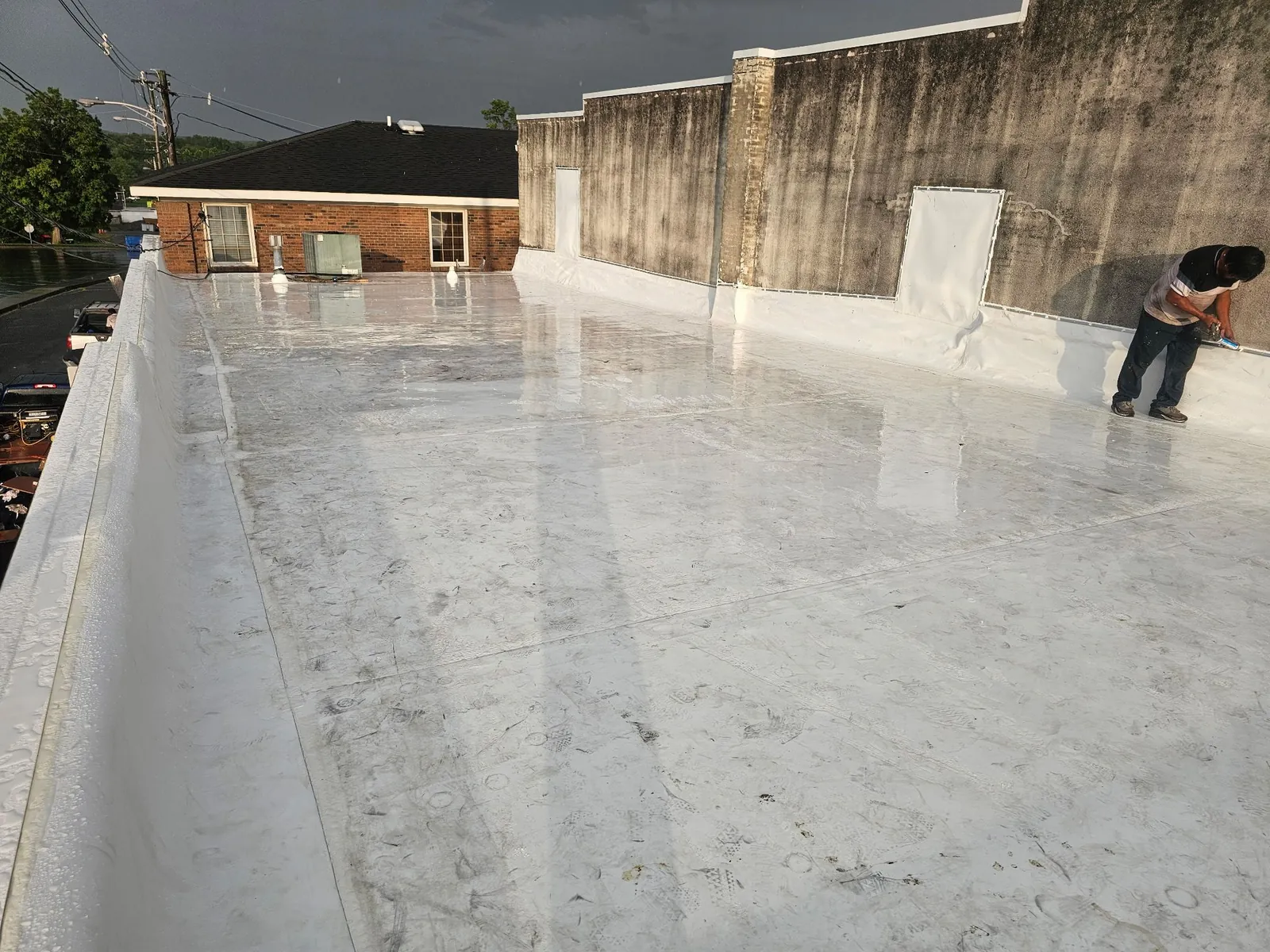 Finished white single-ply membrane roof as a crew member completes the wall flashing