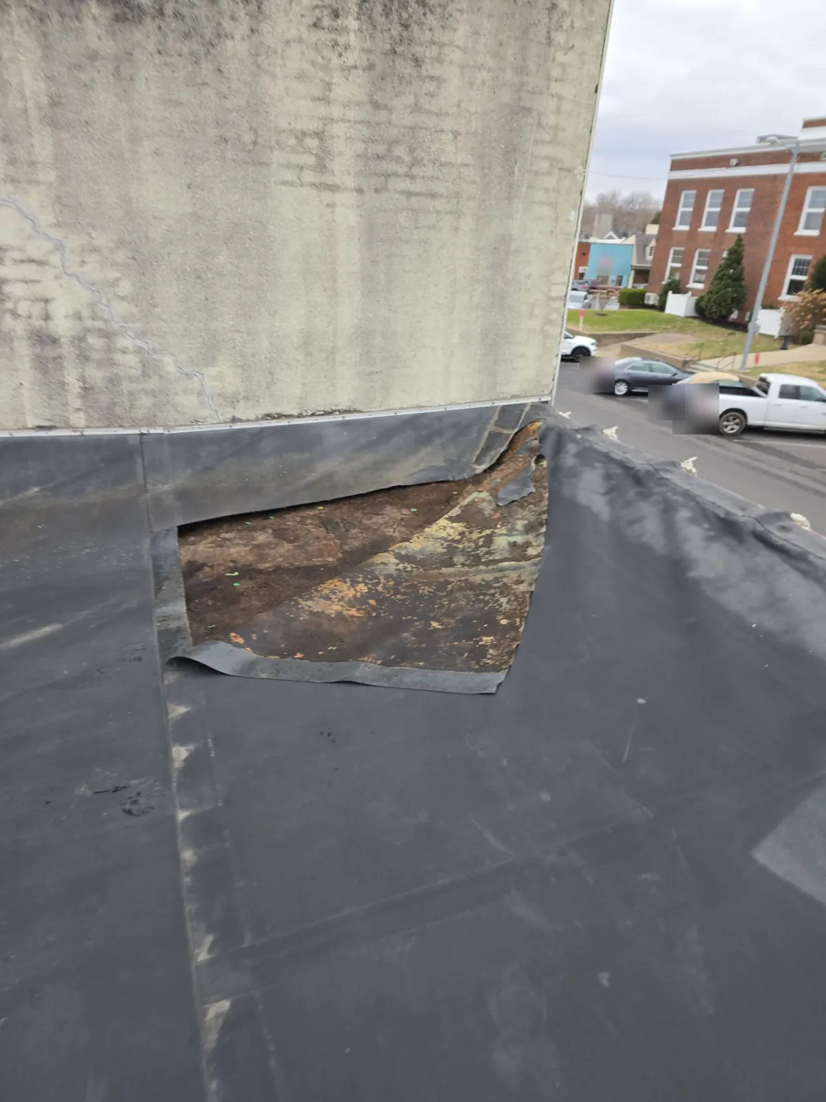 Old flat roof membrane torn away from a masonry wall on a commercial building in Benton, KY, exposing deteriorated material underneath