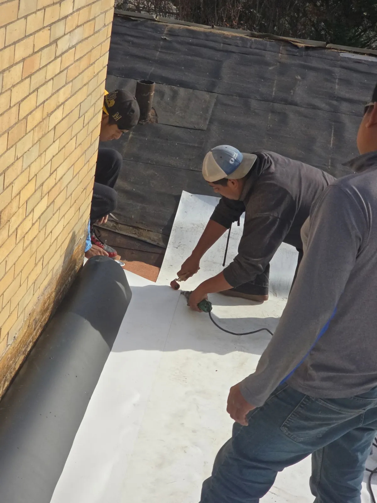 Crew heat-welding white single-ply membrane along the base of the brick chimney
