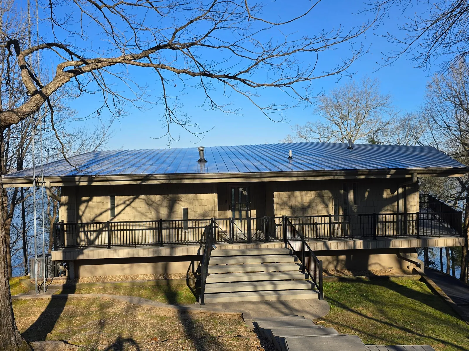 The finished standing-seam metal roof on the lakeside home, framed by bare tree branches