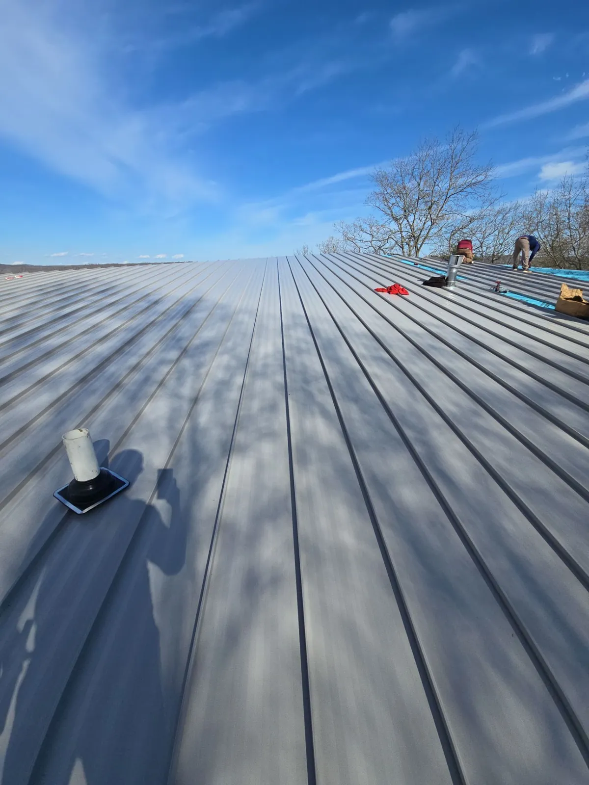 New standing-seam panels with a pipe boot flashing as the crew works near the ridge