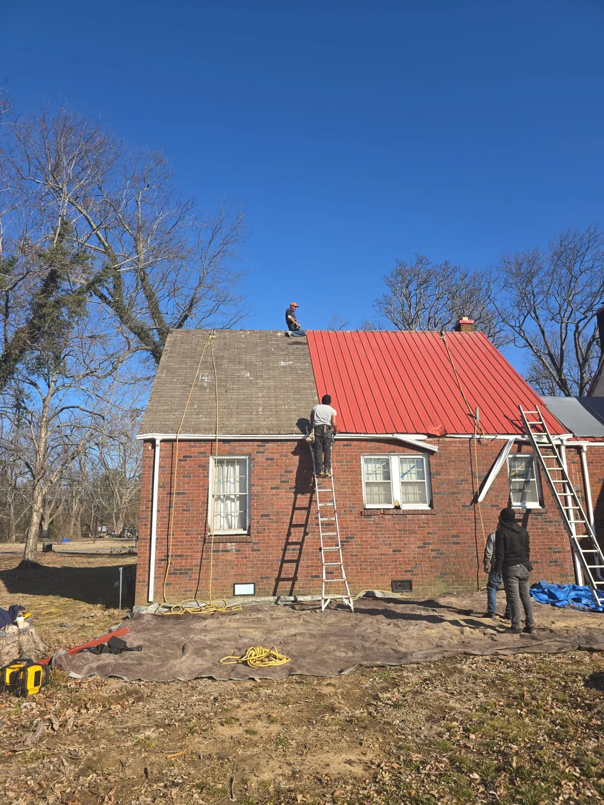 Brick home in Lynn Grove, KY with weathered shingles on one side of a roof section and red metal on the other, as the crew works from ladders and the ridge