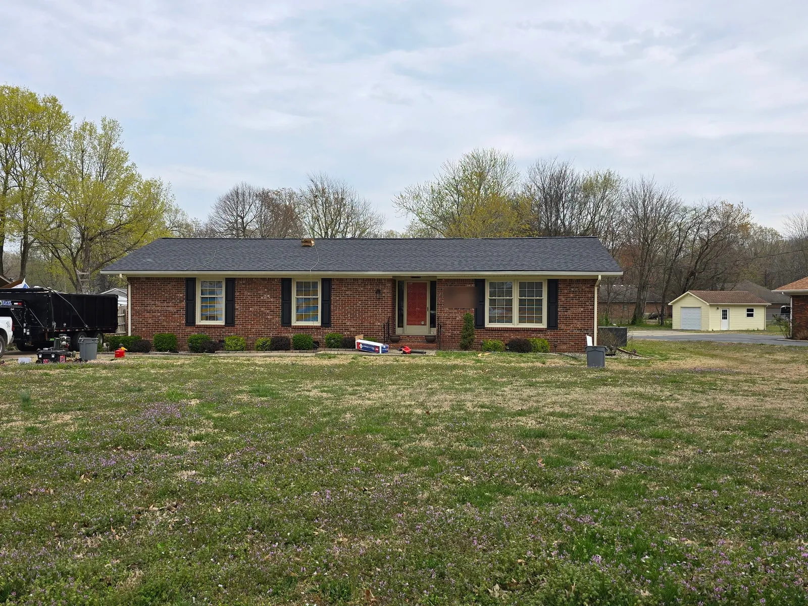 The brick ranch home with its new dark architectural shingle roof, crew equipment still in the yard