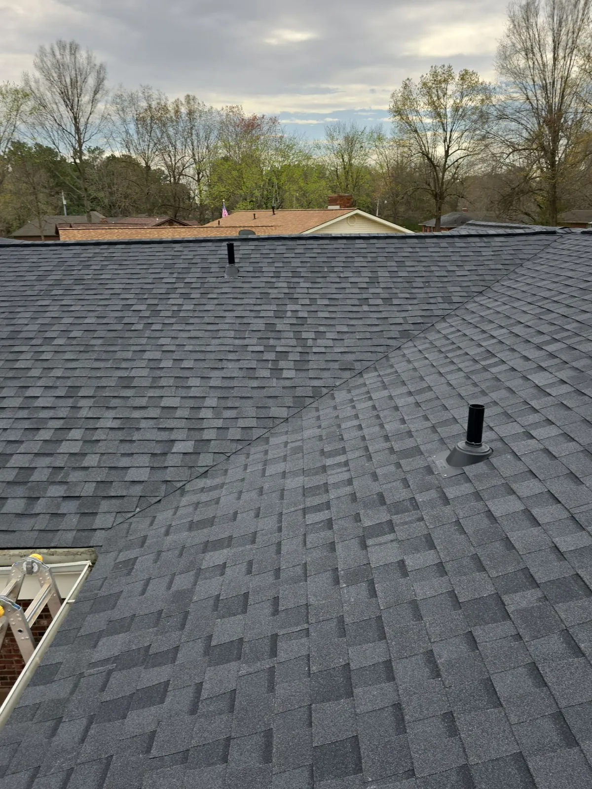 New dark architectural shingles meeting at a valley, with pipe boot flashing on a plumbing vent